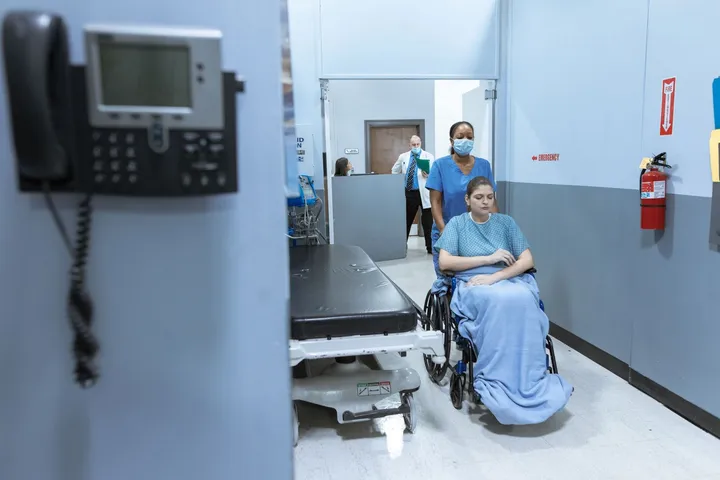 A nurse assisting a patient along a hospital corridor
