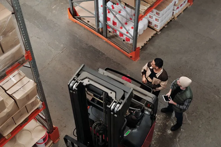 Warehouse staff working beside a forklift and stocked shelves — Avaib