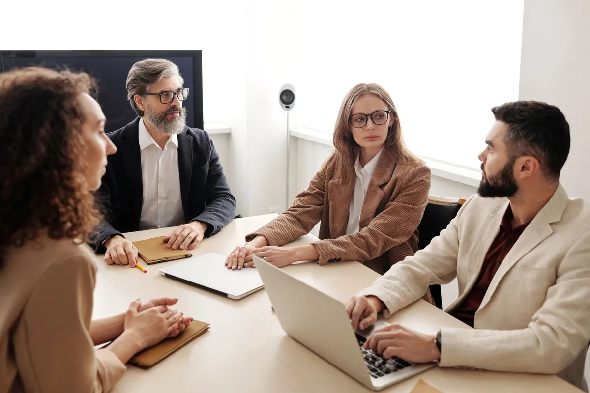 Consultants advising clients around a boardroom table with laptops