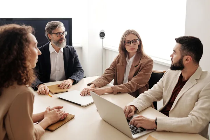 Consultants discussing work around a boardroom table with laptops — Avaib